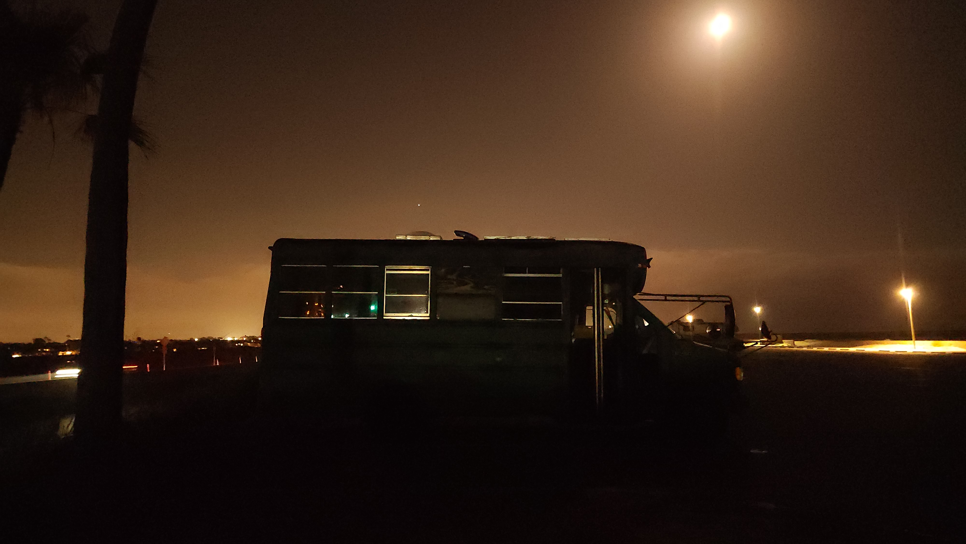 A wide-angle night shot of a school bus tiny home parked under a street lamp with glowing interior lights.